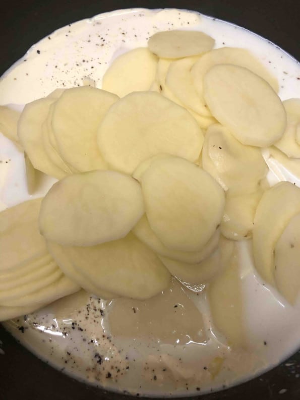 Sliced potatoes added to cream mixture in pot