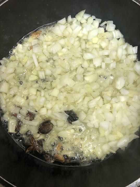 Onions and whole garam masala in ghee in pot