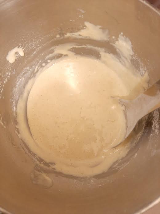 Flour being mixed into egg batter in bowl with metal spoon