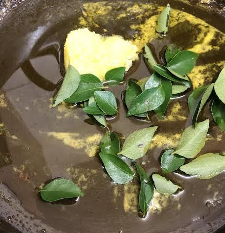 Curry leaves added to oil and ghee in pot