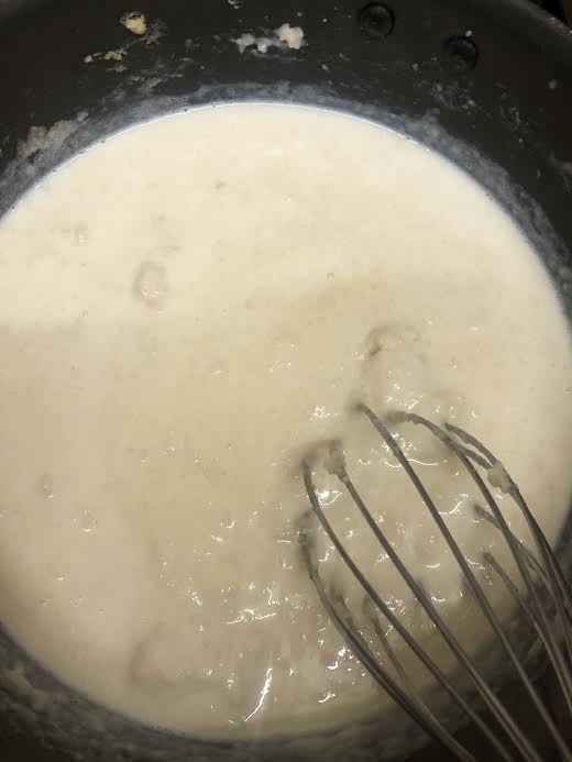 Creamy flour and milk sauce being whisked in pot