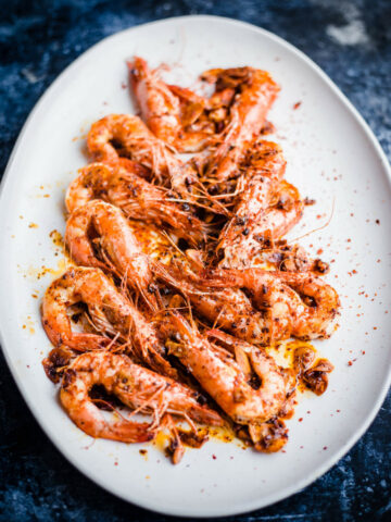 A pile of Chilli Garlic Prawns in a white oval plate