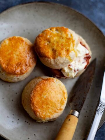 3 scones on a plate with jam and clotted cream