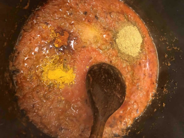 Ground spices added to tomatoes in pot