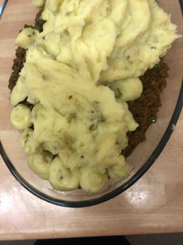 Mashed potato being added on top mixed lamb in casserole dish