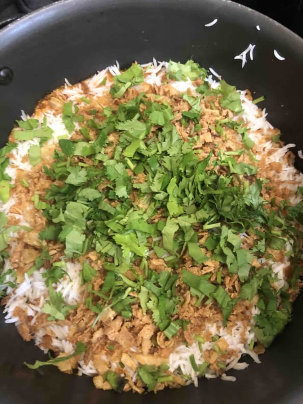 Pot showing top layer of biryani with onions and coriander on top