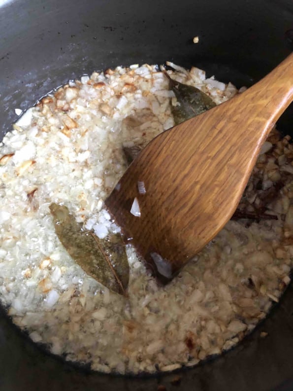 Onions and whole spices in pot with wooden spatula