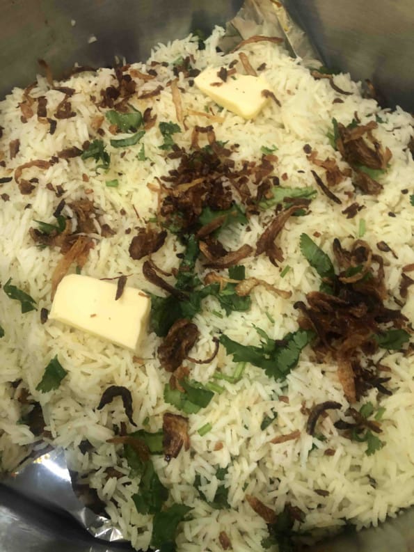 Fried onions, butter and coriander on top of rice layer in pot
