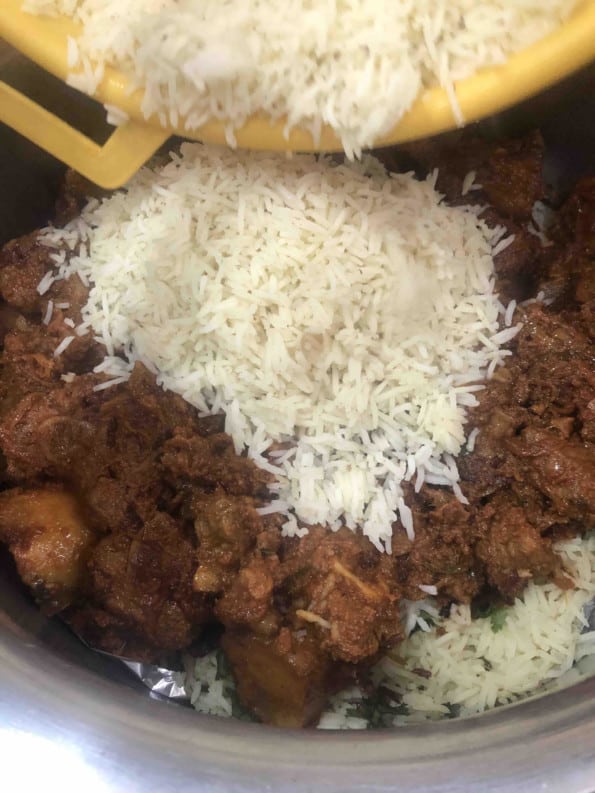 Rice being added on top of lamb in pot