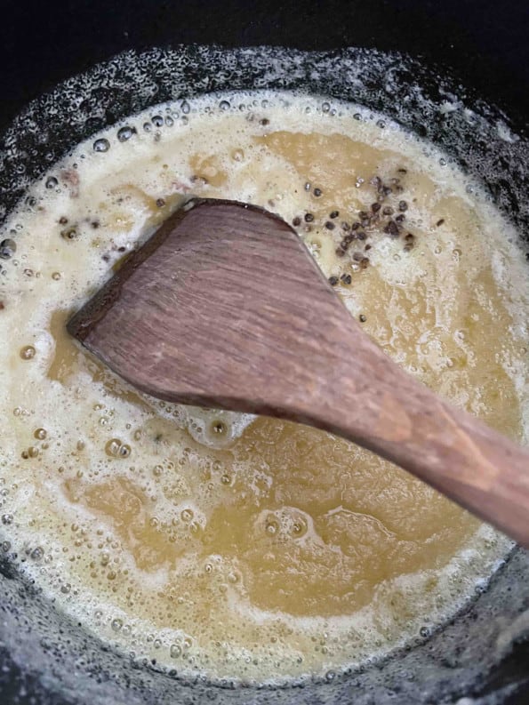 Ghee and Cardamom in pot being stirred with wooden spoon