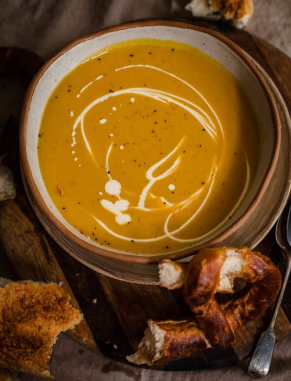 Pumpkin Soup in a bowl with cream drizzled over and pretzels to side