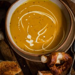 Pumpkin Soup in a bowl with cream drizzled over and pretzels to side