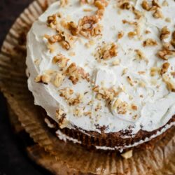 Carrot and Walnut Cake with cheese frosting and chopped walnuts on top on a wooden board