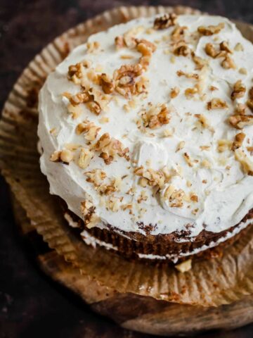 Carrot and Walnut Cake with cheese frosting and chopped walnuts on top on a wooden board