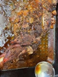 Leg lamb in tin with stock being ladled over the top