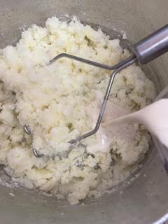 Milk being poured into mashed potatoes in pot