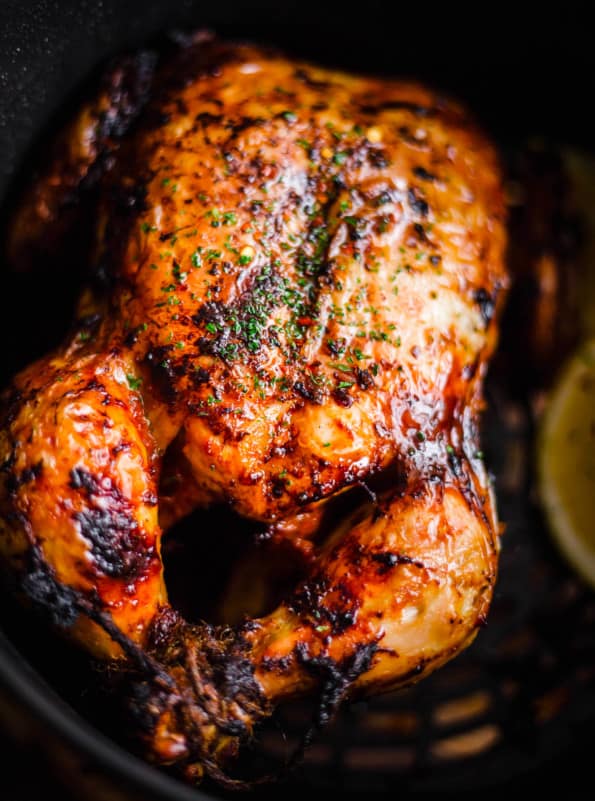  Air Fryer Whole Chicken in air fryer basked with piece of lemon to side