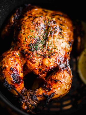 Air Fryer Whole Chicken in air fryer basked with piece of lemon to side