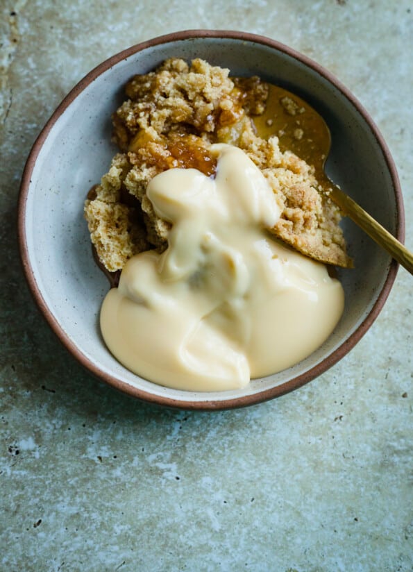 Pear crumble and custard in a bowl with a spoon