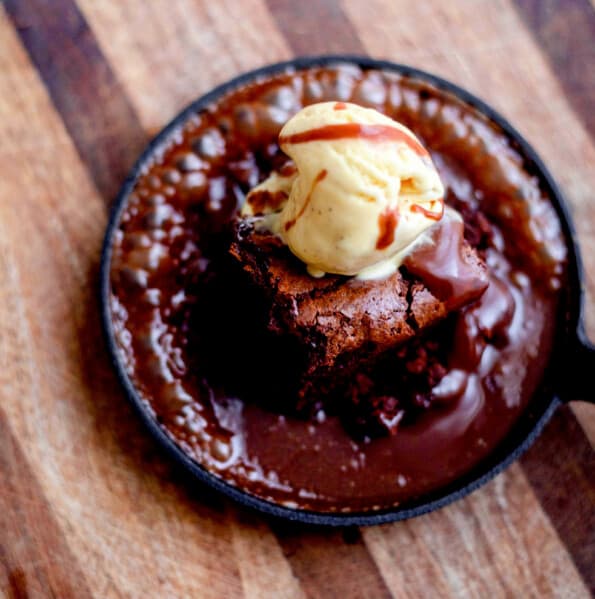 Chocolate brownie with bubbling chocolate sauce and ice cream in a cast iron pan