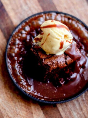 Chocolate brownie with bubbling chocolate sauce and ice cream in a cast iron pan