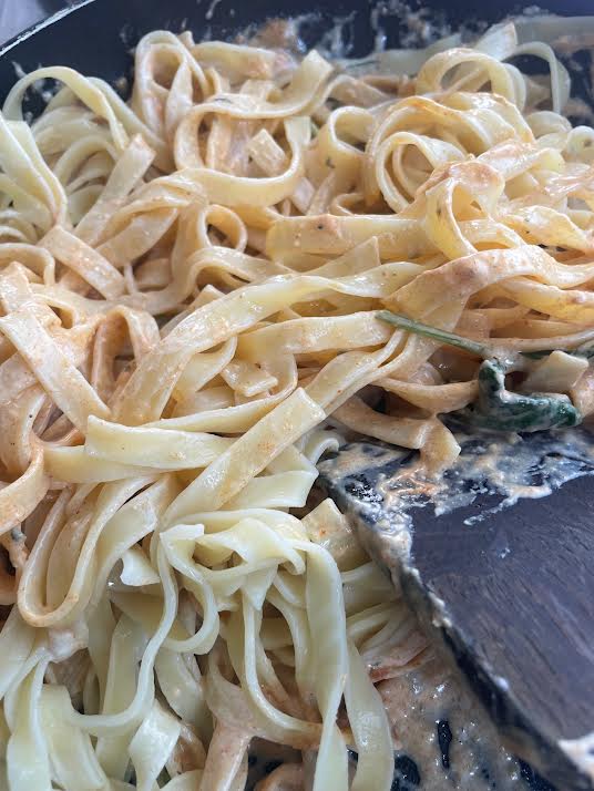 Pasta added to creamy sauce in pan
