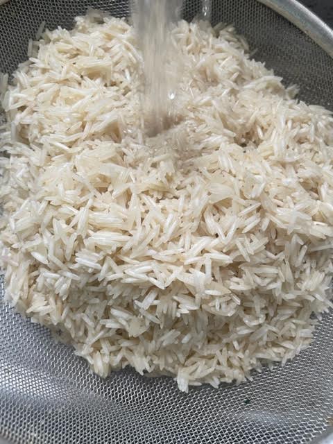 basmati Rice in colander being mashed under tap water