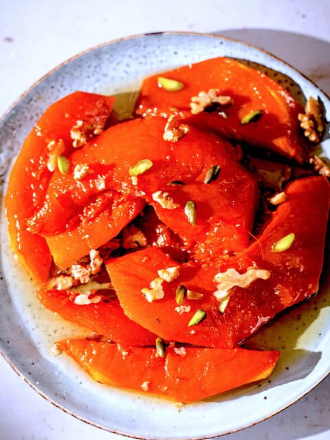 Caramalised pumpkin wedges in plate with syrup and walnuts