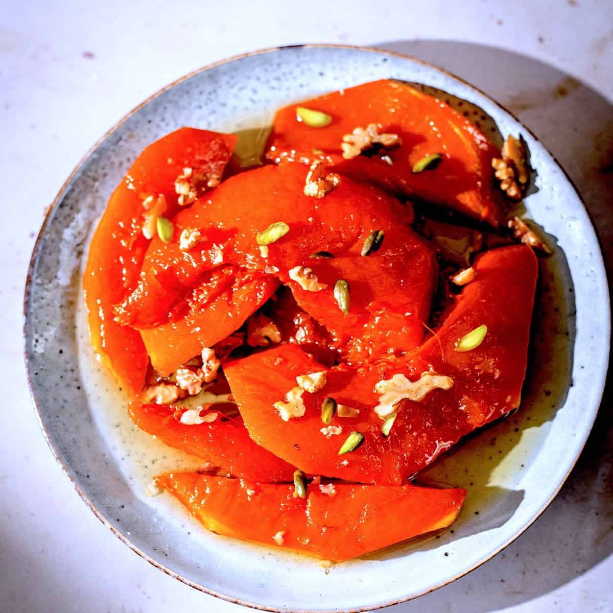 Caramalised pumpkin wedges in plate with syrup and walnuts