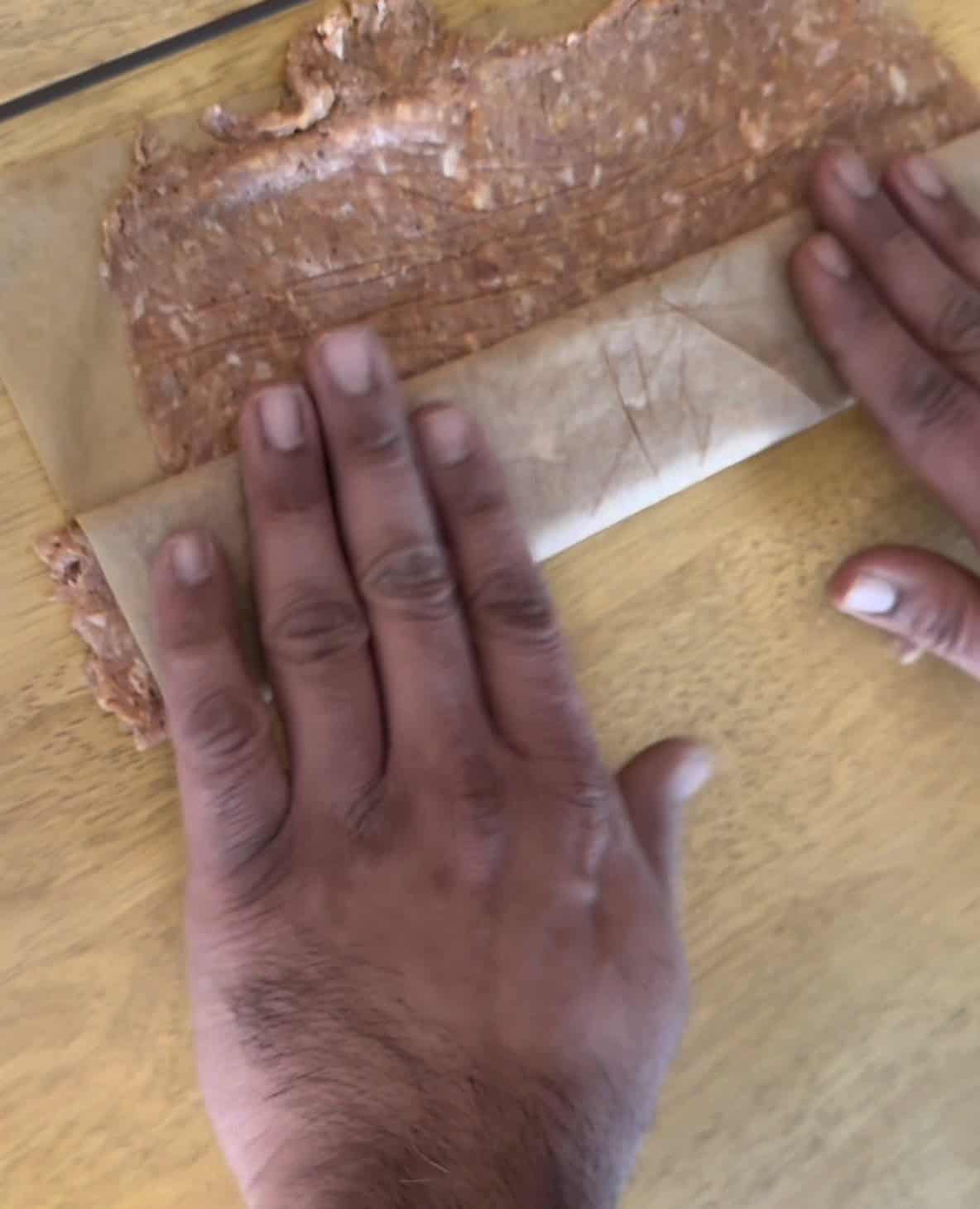Kebab mixture being rolled between 2 bakign paper pieces