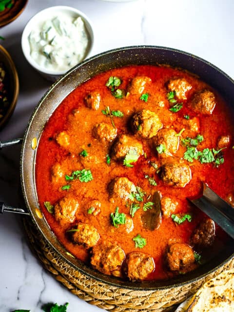 Kofta curry in pot with salads and chapatti to side