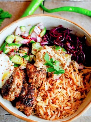 Kofta, rice, hummus, salad, tahini sauce and pickles in bowl